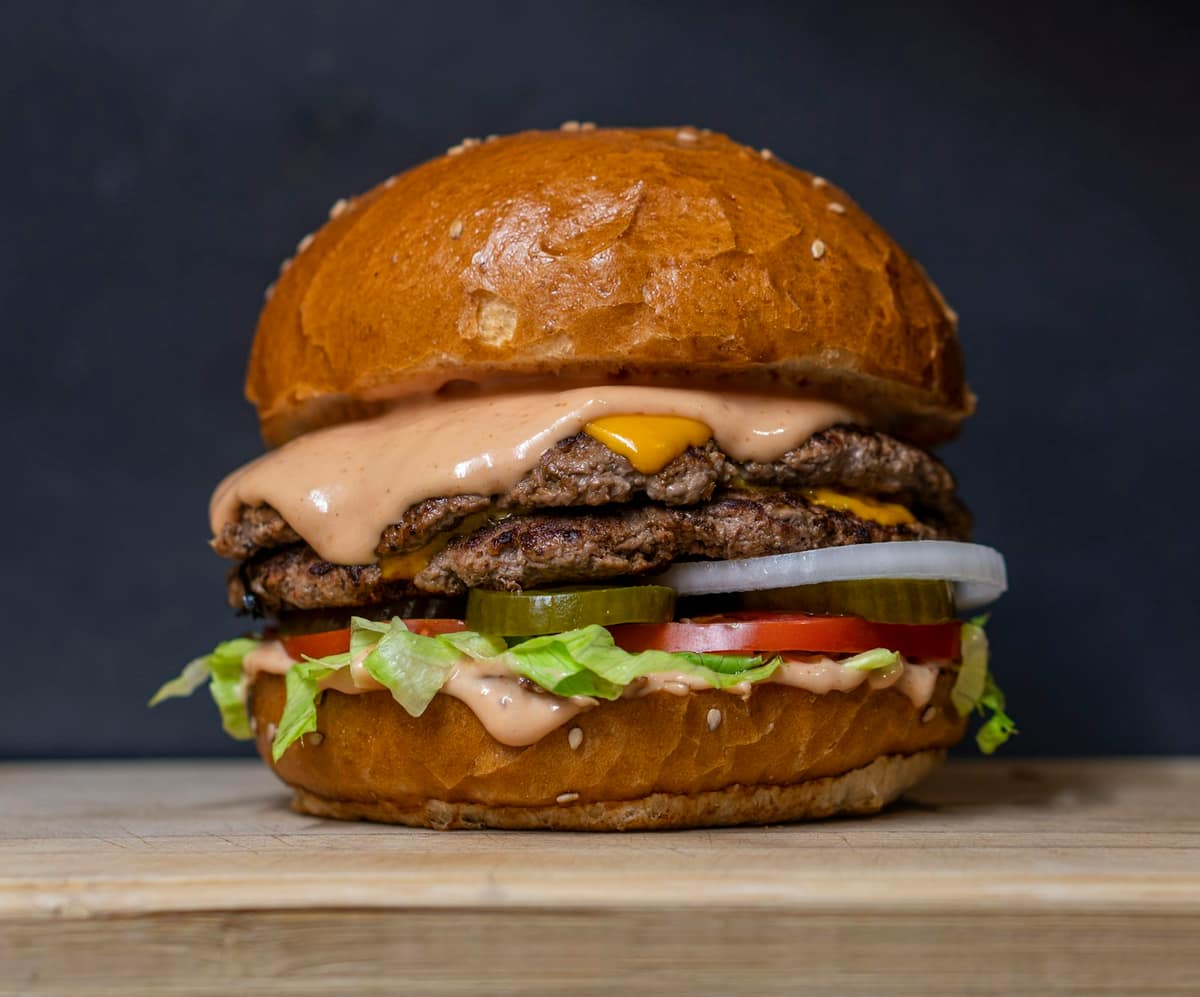 Hamburguesa doble con queso fundido, salsa y vegetales frescos en pan de sésamo sobre tabla de madera
