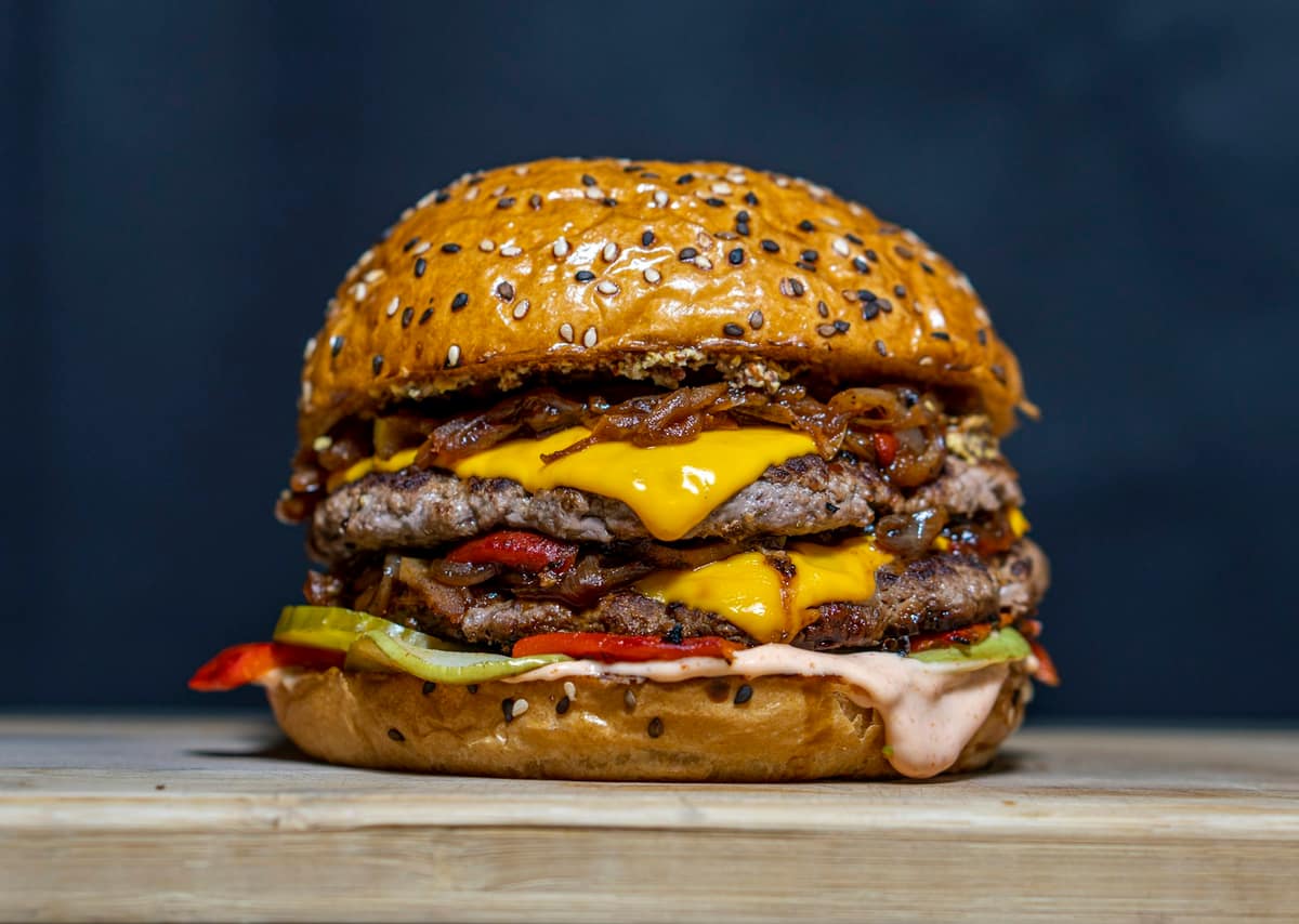 Hamburguesa doble con queso cheddar derretido y cebolla caramelizada en pan con semillas de sésamo, fondo oscuro