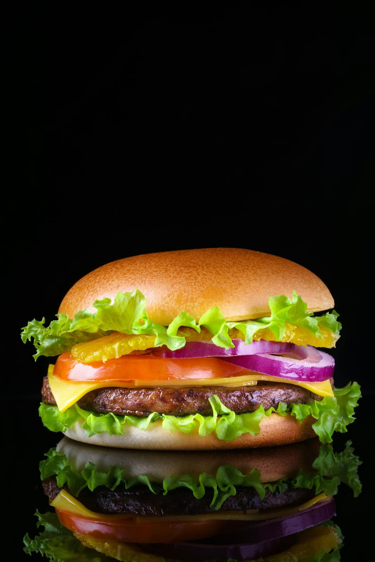 Hamburguesa con queso y vegetales frescos reflejada sobre una superficie negra, fondo negro
