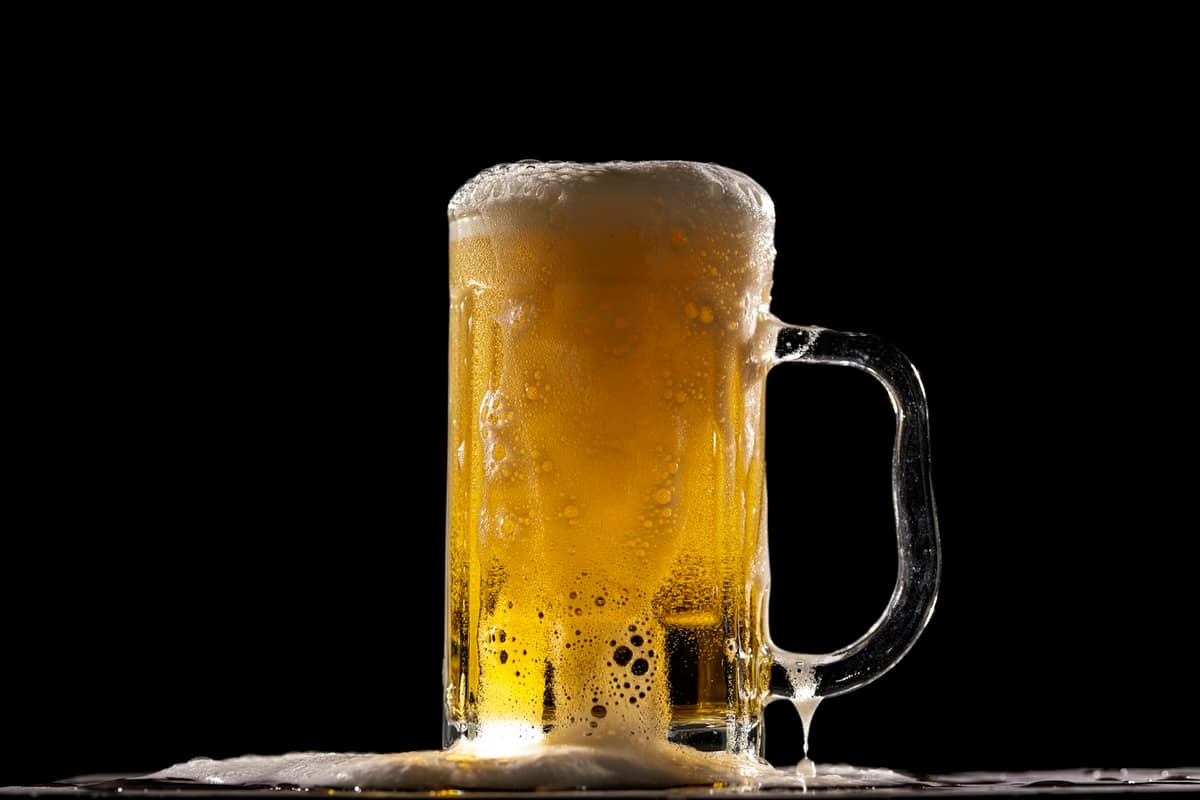 Cerveza dorada con espuma desbordante sobre fondo negro