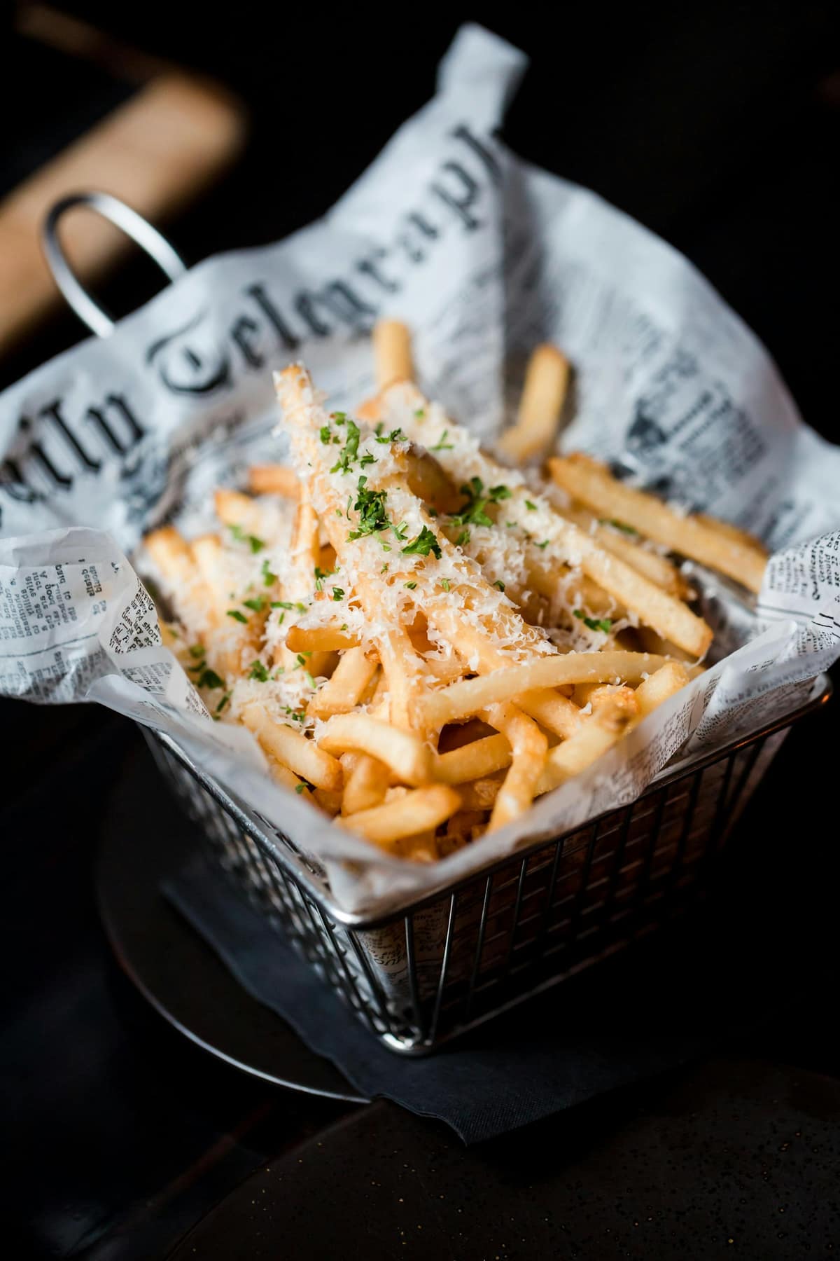 Papas fritas en una cesta metálica forrada con papel, ambiente oscuro