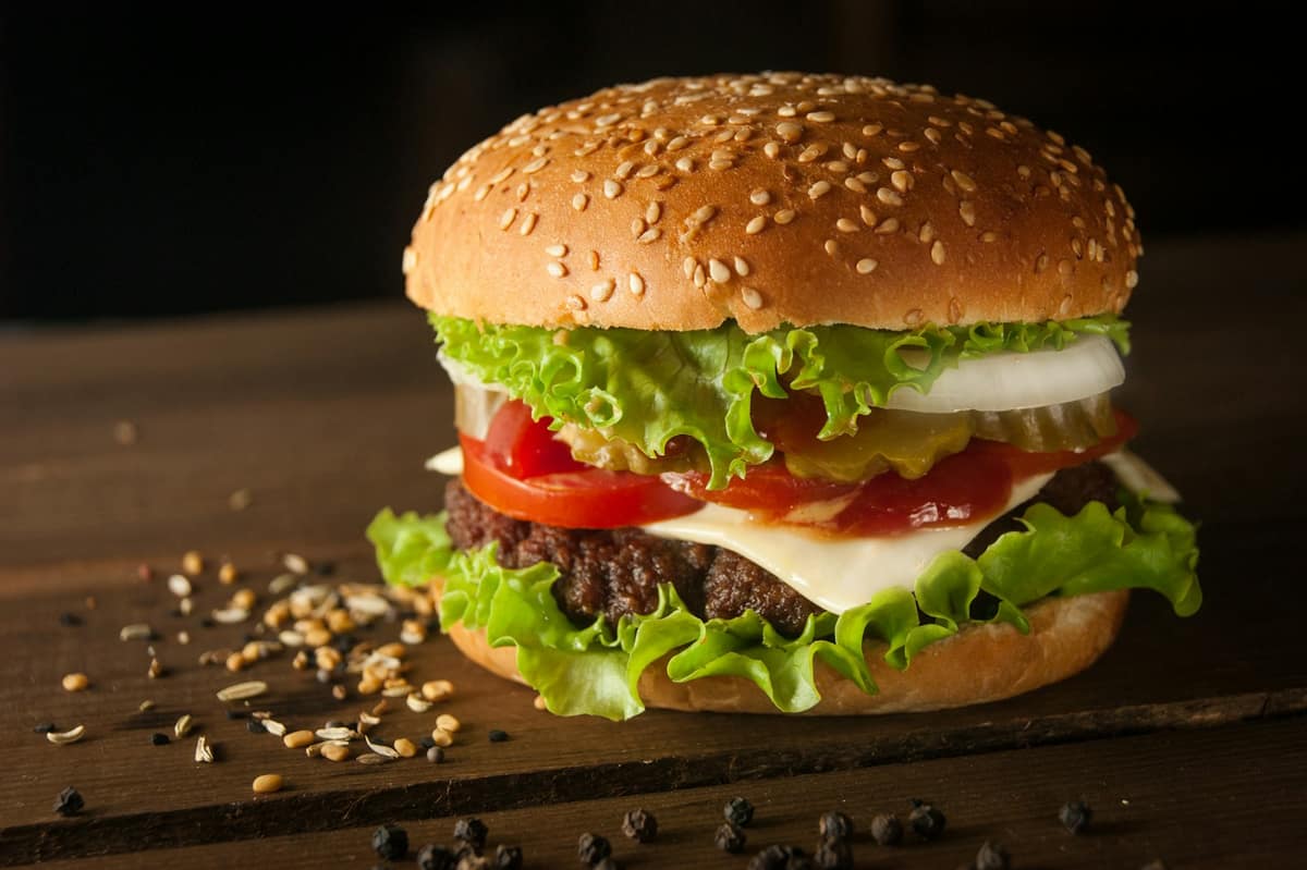 Hamburguesa con medallón especiado, queso, tomate y lechuga en pan con semillas de sésamo sobre mesa de madera