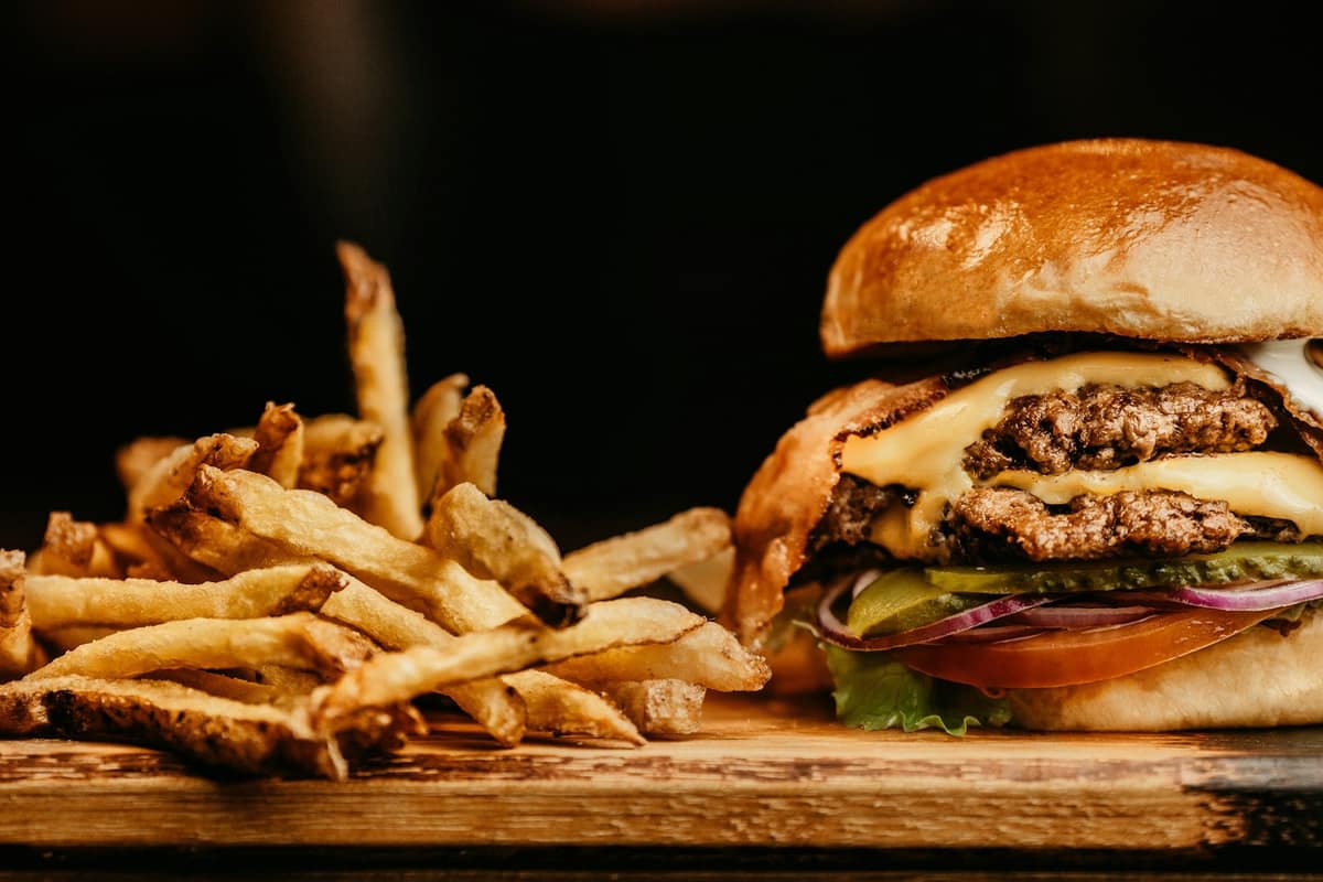 Hamburguesa doble con queso junto a papas fritas caseras sobre tabla de madera con fondo oscuro