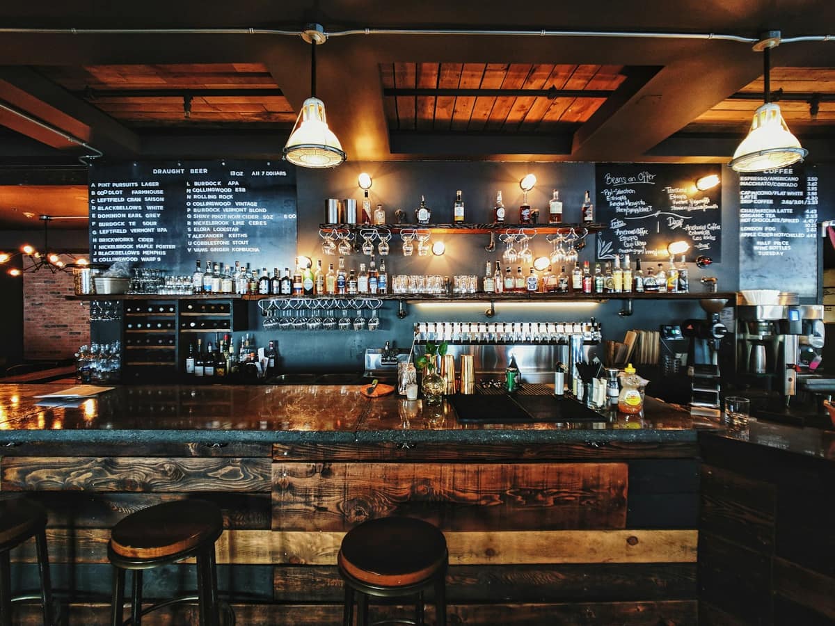 Barra de bar con taburetes, pizarras con la carta de cervezas y estantes de botellas bajo una iluminación cálida